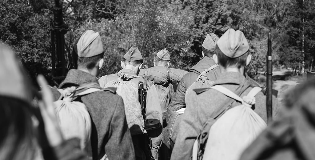Re-enactors dressed as WWII soldiers marching through forest.