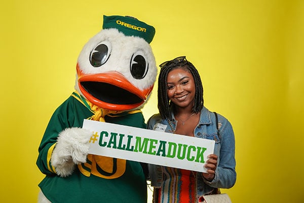 Student poses with The Duck while holding a sign that says #CallMeADuck