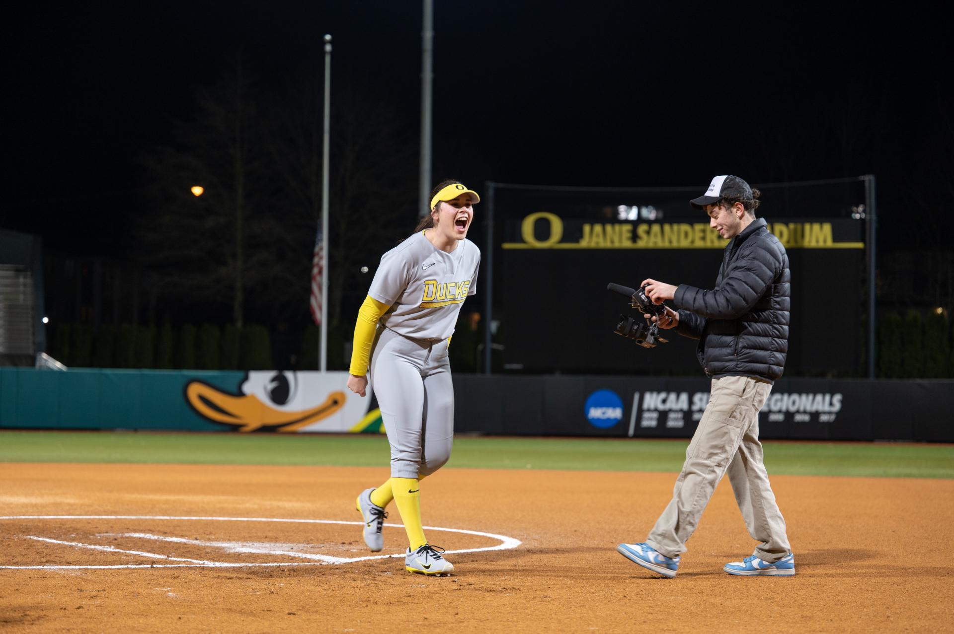 Softball player on a night field as a videographer films near home plate during a game.