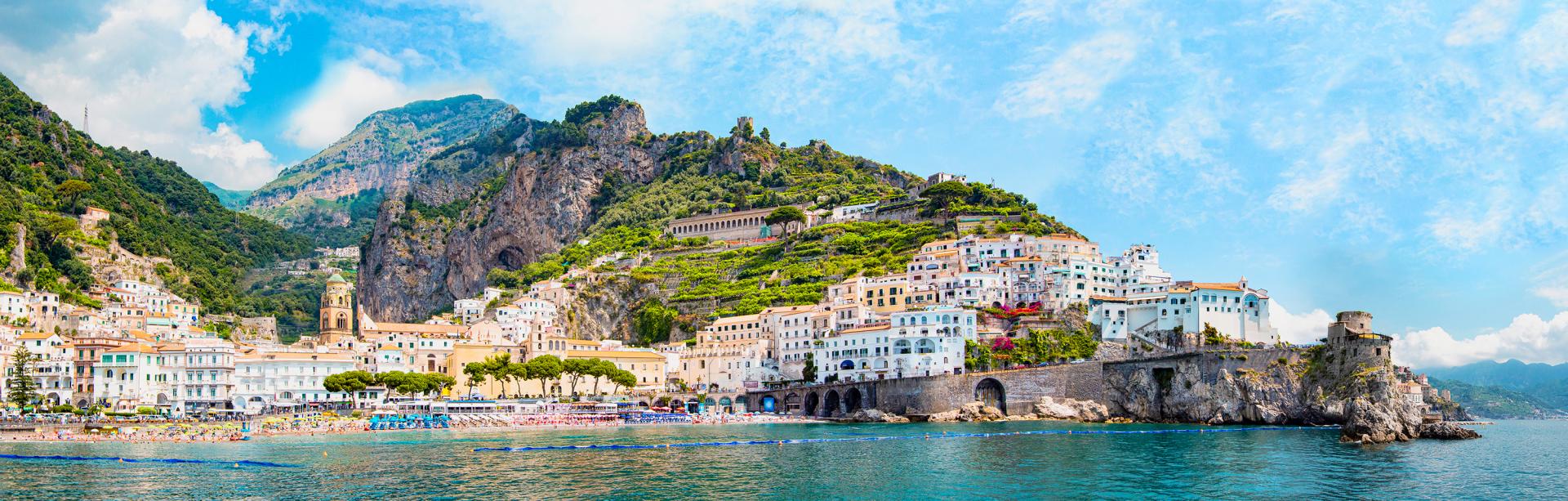 White buildings line the cliffs and waterfront of green and gray hills above turquoise waters.