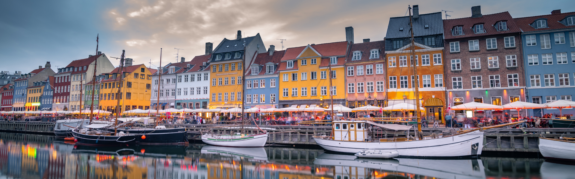 Yellow, blue and red, buildings line the waterfront along a river with boats.