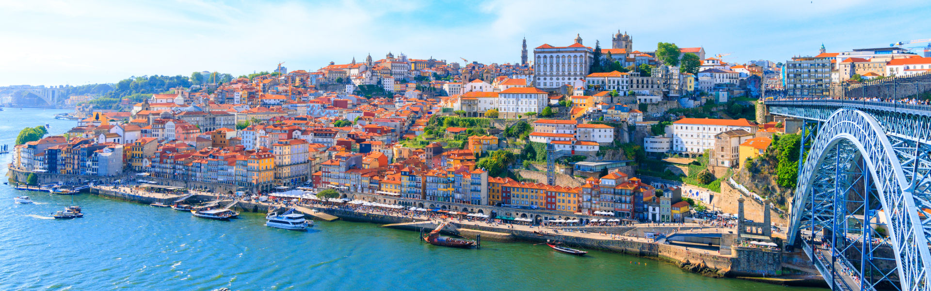 Red-roofed buildings cluster beyond a blue river into the horizon of a blue sky.