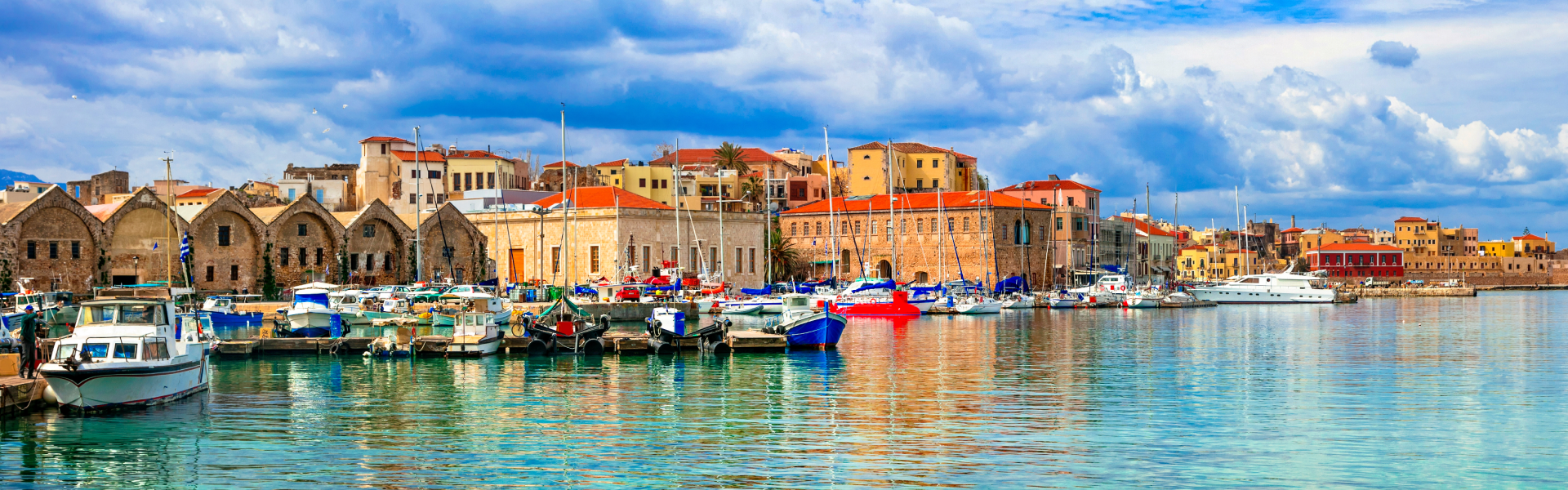 Clear turquoise waters and a cloudy blue sky sandwich orange and tan buildings along the waterfront.