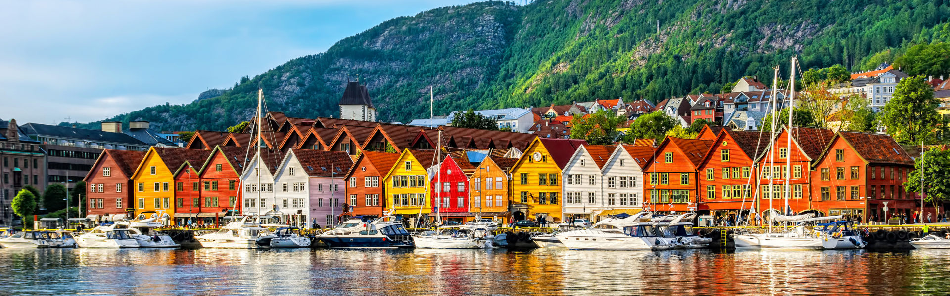Red, yellow, and orange buildings line the waterfront below green mountains.