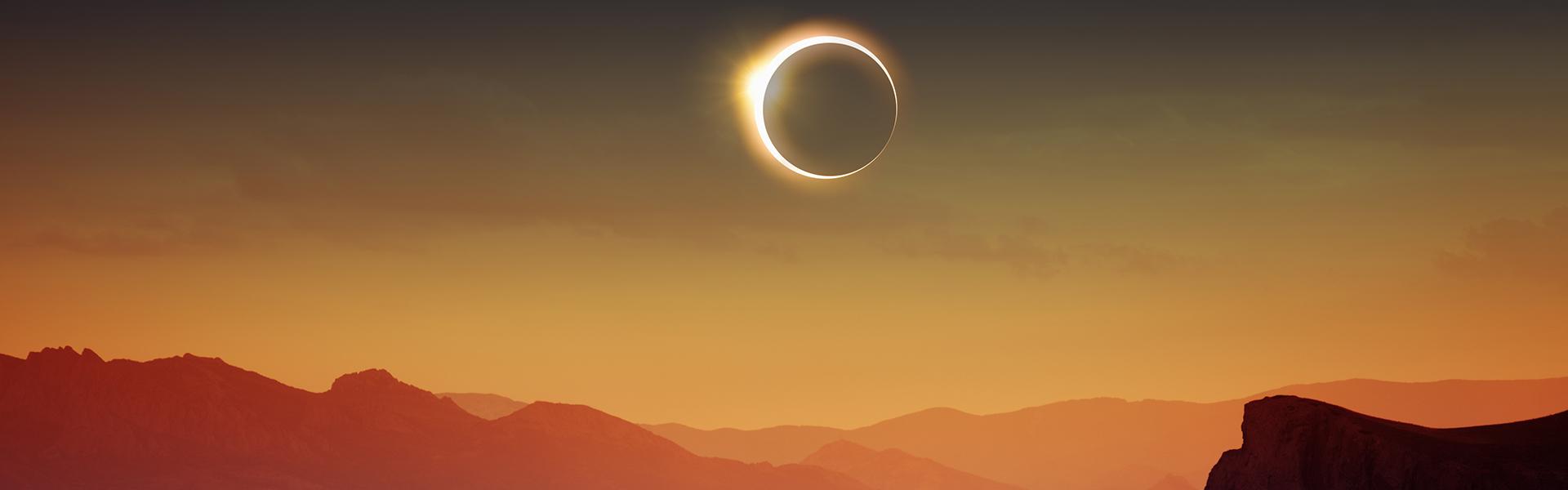 A solar eclipse above the tops of mountains in an orange sky.