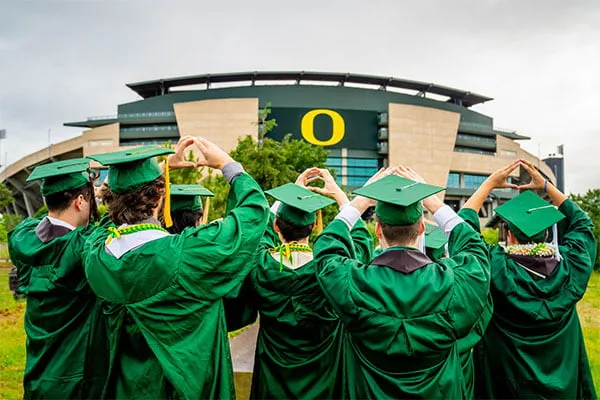 Group of grads throw their O in their cap and gowns outside Autzen