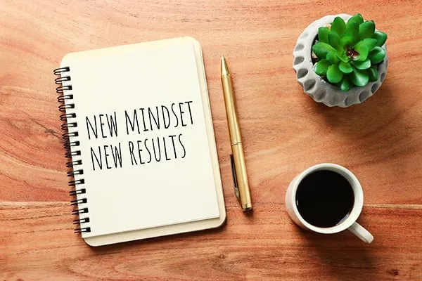 Notebook that says New Mindset New Results with coffee cup and succulent on a table
