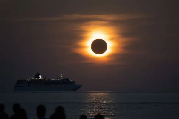 A cruise ship sits on the horizon during a solar eclipse.