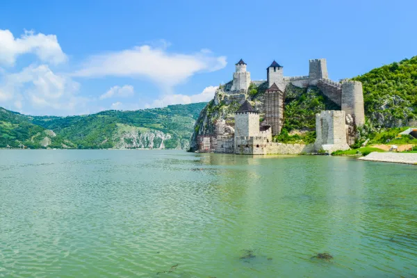 Blue waters ripple below a hillside castle with gray stone towers jutting up from the green hills.