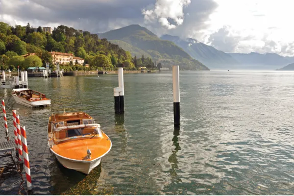Small boats anchored to the docks sit on the rippling water, European mountains fading into the background.