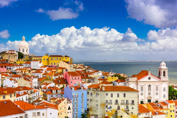 The colorful buildings of pink, blue, yellow, green, and more expand towards the horizon of Lisbon while fluffy clouds and the ocean sit beyond.