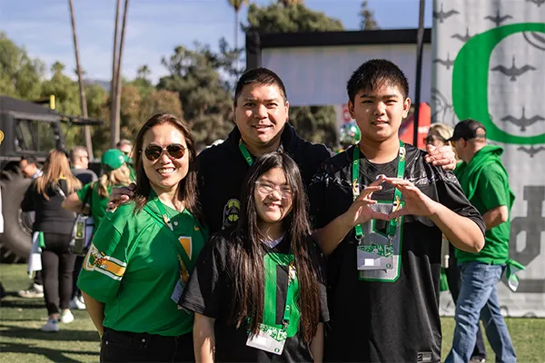 Four people standing outdoors wearing green and black shirts with lanyards.