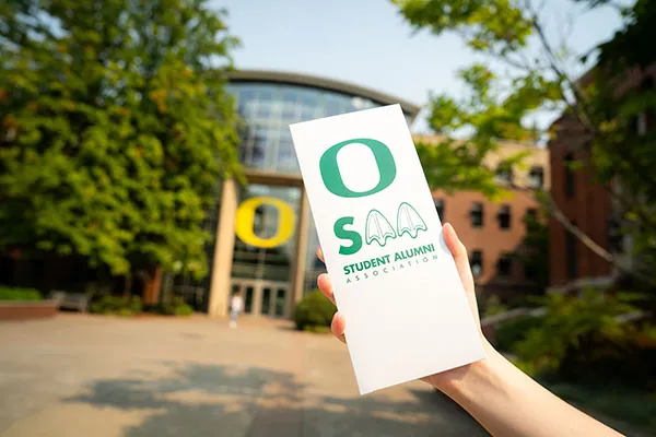 A person holding a pamphlet that reads, "Student Alumni Association."