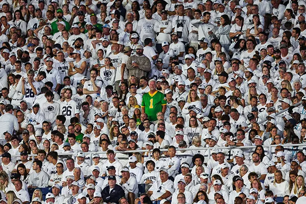 A man wearing a bright green UO jersey stands among a sea of Penn State fans all wearing white.