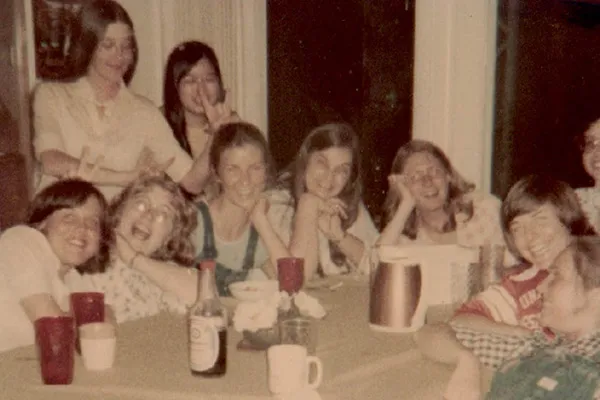 Jenny Bender, Sharon Bryan, Karen Coon, Susan Scovil, Mary Jo Kealy, Cat Weber, Faye Blumenthal, Patty Pavel Lentz, Lexie Caswell, and Susan Ota around a table smile at the camera with red cups and white mugs in front of them.