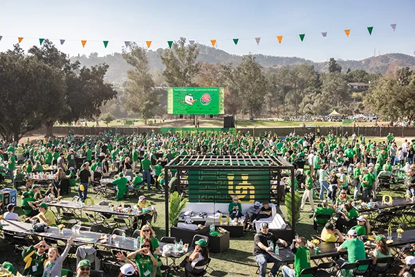 A large group of University of Oregon Ducks fans gathering in an event space wearing Ducks gear. 