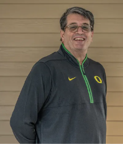 Fred Poust smiles at the camera in a dark gray Oregon pullover.