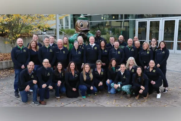 A group photo of the University of Alumni Board Members pose in front of a Duck statue and a modern building.
