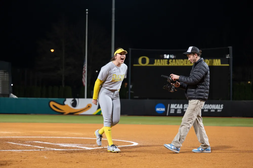 Softball player on a night field as a videographer films near home plate during a game.