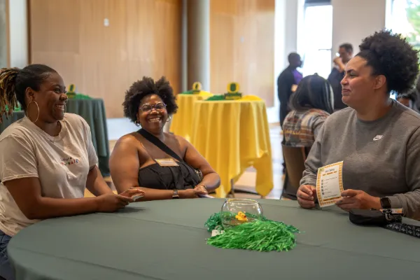 Three Black UO alumni sit around a table together talking.