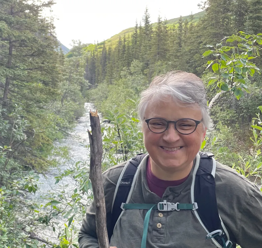 Jennie Bricker headshot in front of a river and evergreen trees.