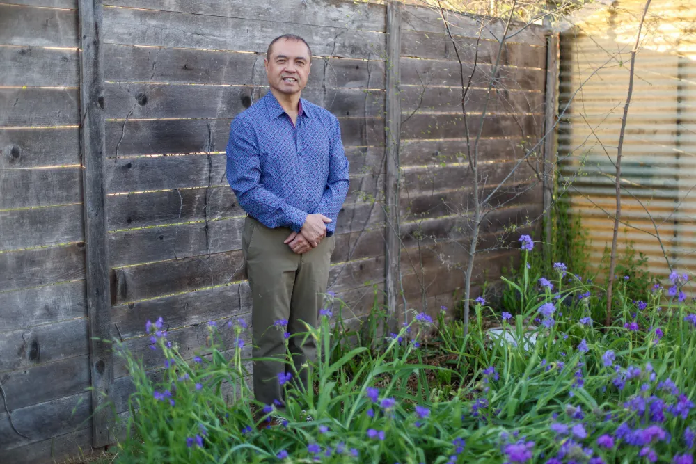 Luis Carcamo-Huechante stands in front of a fence among purple flowers in a blue button up shirt and khakis.