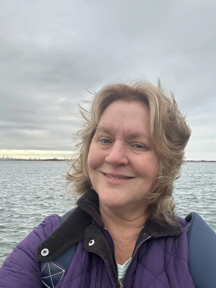 CJ Lake, a blonde white woman takes a selfie with a lake behind her.