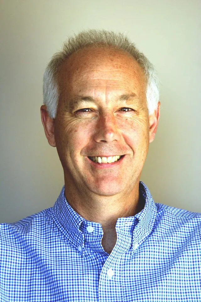 Headshot of Kevin Johnston, a white man with white hair wearing a blue button up shirt and 
