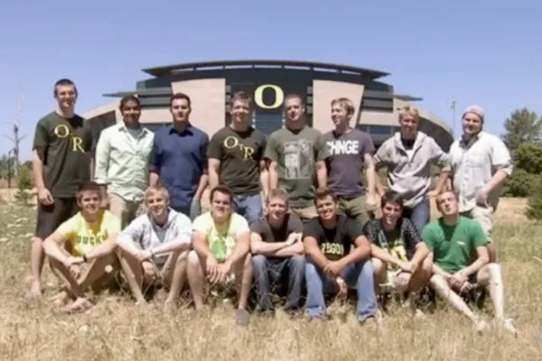 Fifteen young men in the a cappella group On the Rocks stand and sit in two rows for a photo in front of Autzen Stadium, with the yellow Oregon O in the background.