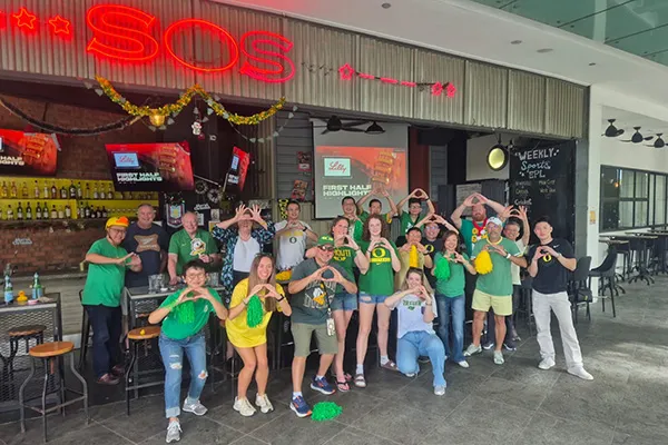 A group of people in Oregon Ducks merch make O shapes with their hands in front of a bar.