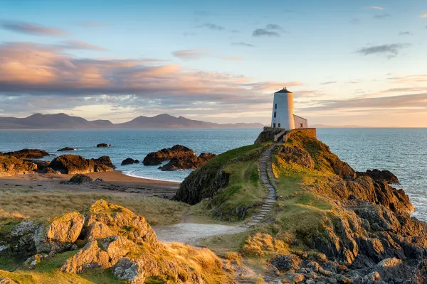 A white stone structure stands on the green edge of a cliff overlooking waters at sunset.