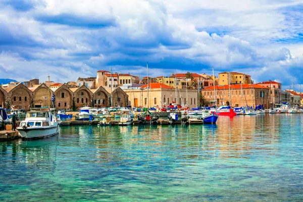 Clear turquoise waters and a cloudy blue sky sandwich orange and tan buildings along the waterfront.