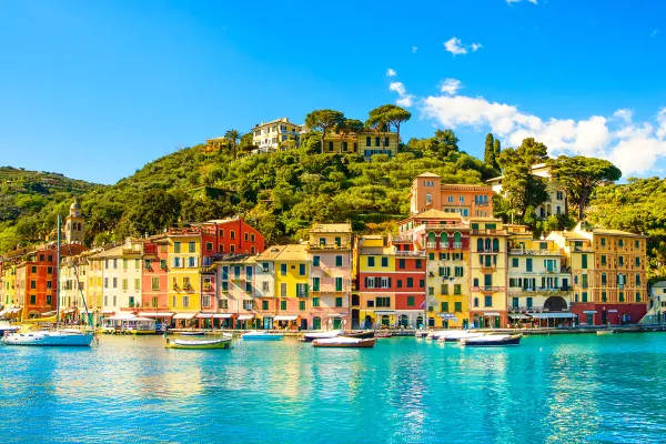 Turquoise waters below multicolored houses on a green tree-covered hillside.
