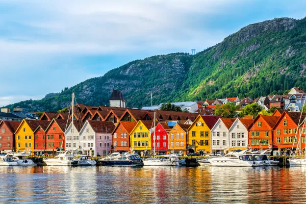 Red, yellow, and orange buildings line the waterfront below green mountains.
