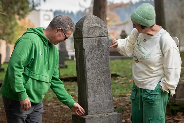 Two people in long-sleeve shirts tend to a gravestone in the Eugene Pioneer Cemetery.