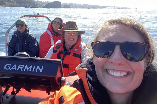 A woman in a life vest and sunglasses takes a selfie with three other people on a boat on the water.