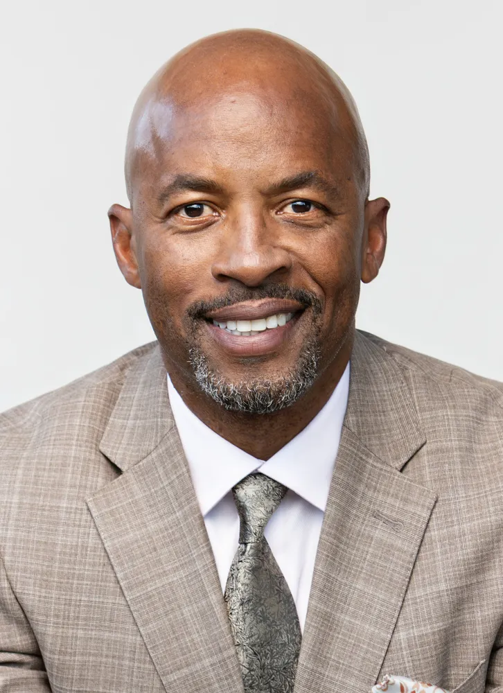 A headshot of J.J. Birden, a Black man in a light brown suit.