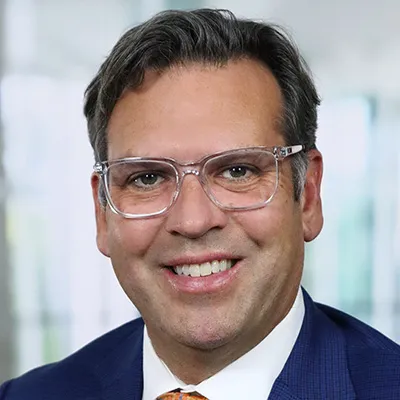 A headshot of Mark Bergeron, a man in a suit and clear-framed glasses.