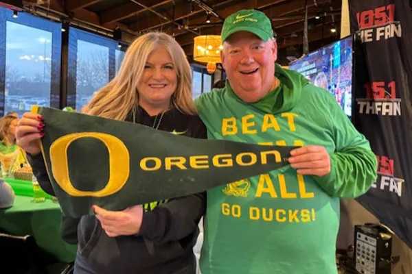 A man and woman in green Oregon gear hold up a University of Oregon pennant.