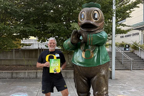 Darren Des Roches holds an orientation packet next to a statue of the Oregon Duck on the University of Oregon campus.