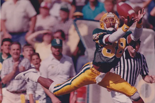 A photo of JJ Birden, a Black man in a 1980s UO Ducks uniform, catching a football.