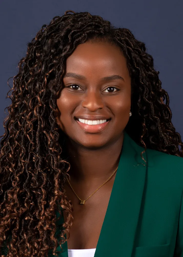 Maneulla Tshala, a Black woman with long black hair and a dark green blazer.
