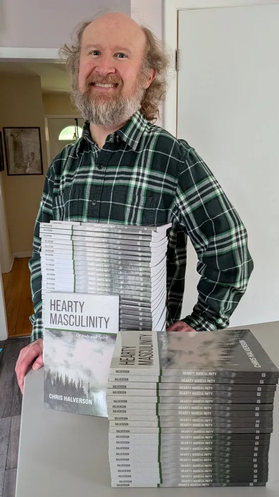 Chris Halverson stands next to a stack of gray and white books smiling.