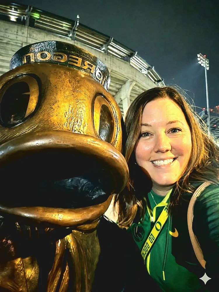 A selfie of Heather Jones with a statue of the Oregon Duck outside Autzen Stadium at night.