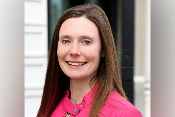 A headshot of a white woman in a pink jacket.