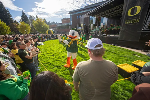 The Oregon Duck stands in front of a crowd of people in front of a stage.