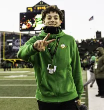 A person at a Football game wearing University of Oregon gear signaling a peace sign. 