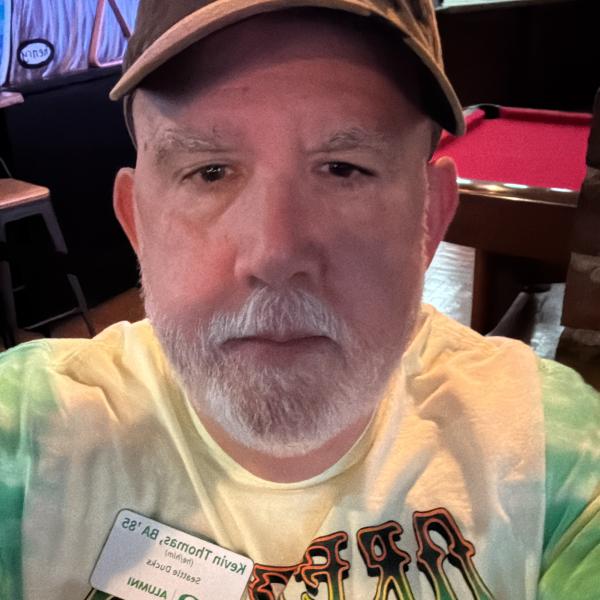 Kevin Thomas wears a green and yellow tie dye Grateful Ducks shirt and a brown hat in a selfie.