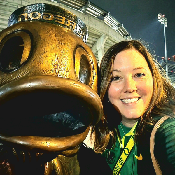 A selfie of Heather Jones with a statue of the Oregon Duck outside Autzen Stadium at night.