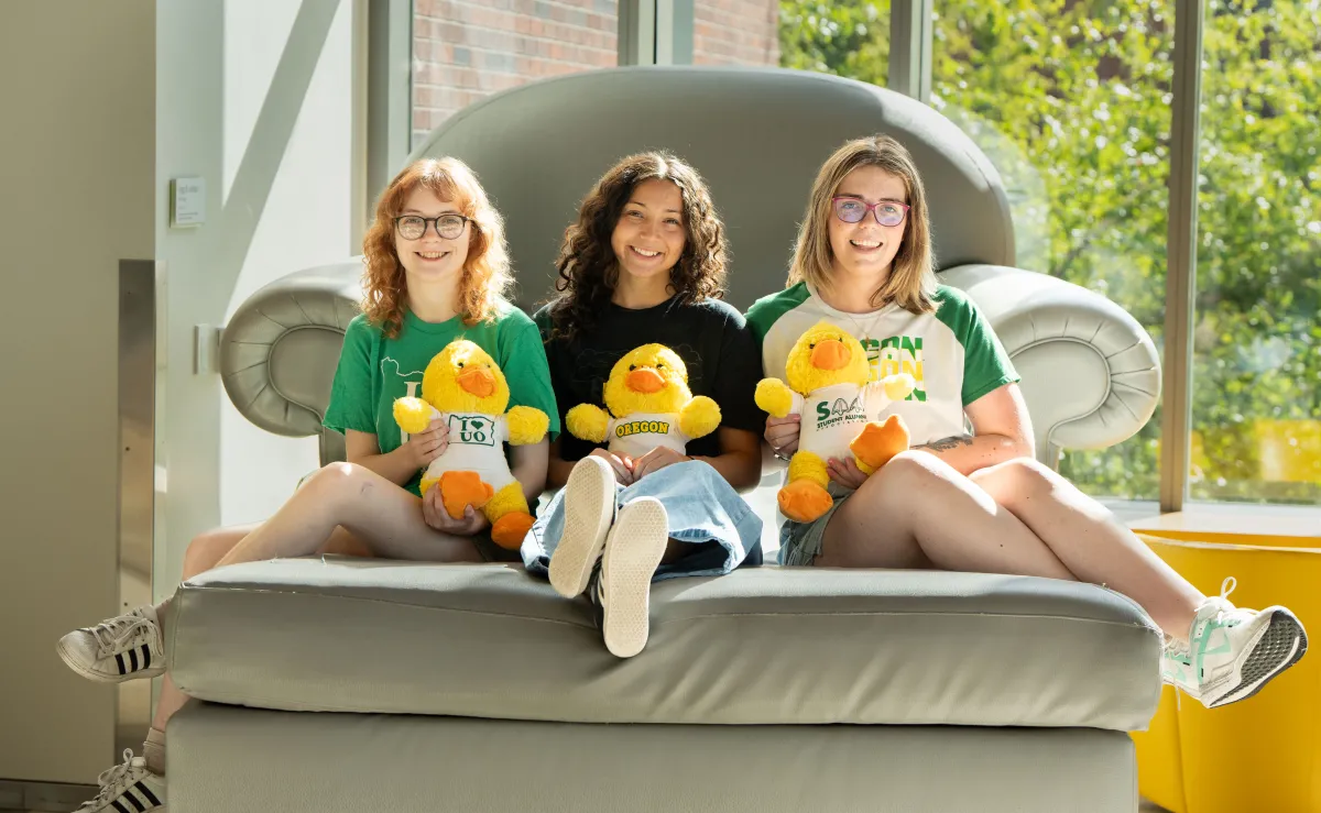 Three female University of Oregon students holding plush duck mascots